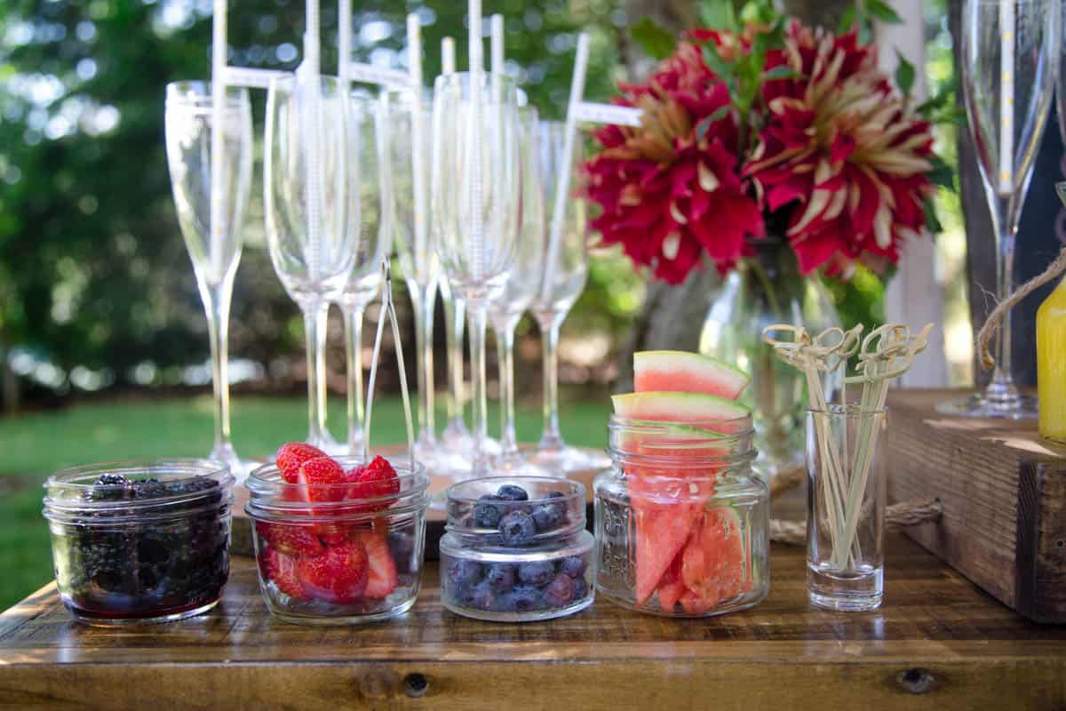 Containers full of fresh fruit on a wood tray with sparkling wine flutes in the background