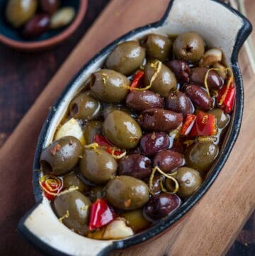 Grilled olives warmed up with garlic and hot peppers in a baking dish on a cutting board.