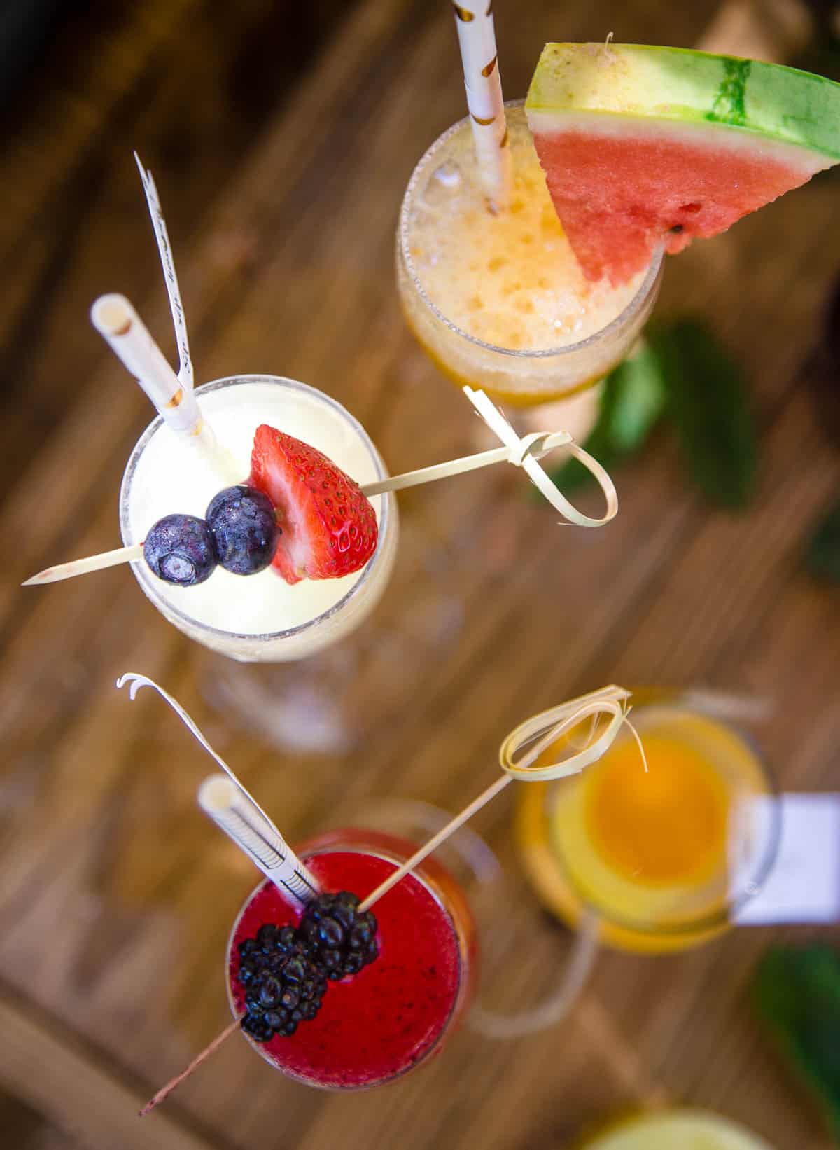 Looking down at three different styles of sparkling wine cocktails with fresh fruit garnishes