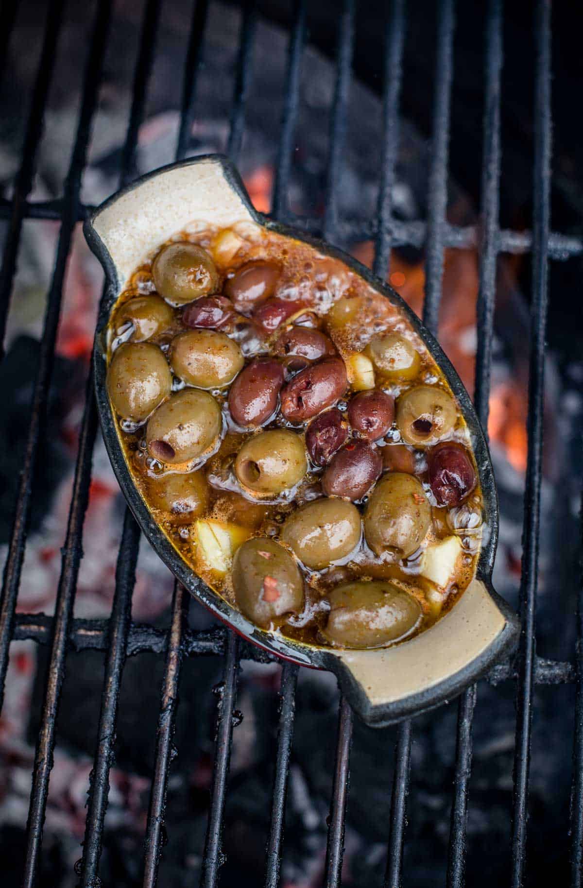 Olives in a baking dish being grilled on a big green egg over direct heat.