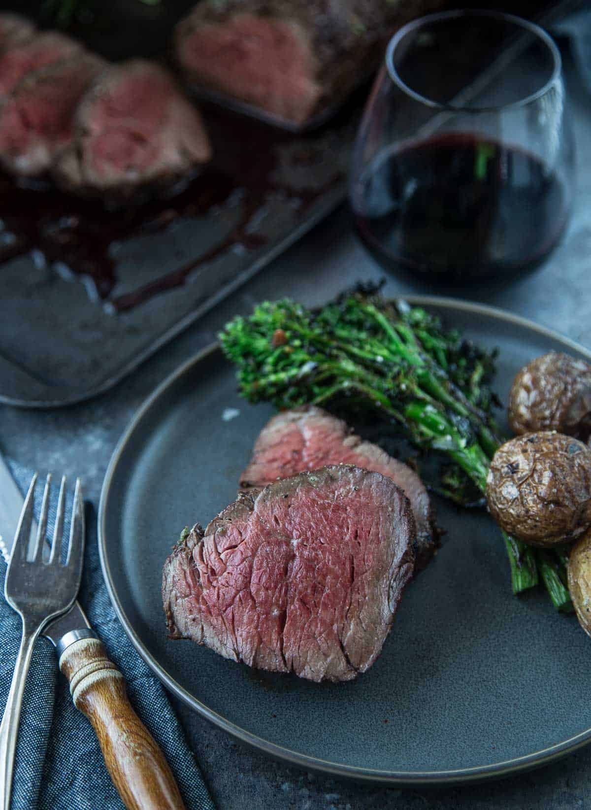 Slices of Smoked Beef Tenderloin on a plate with a glass of red wine on the side