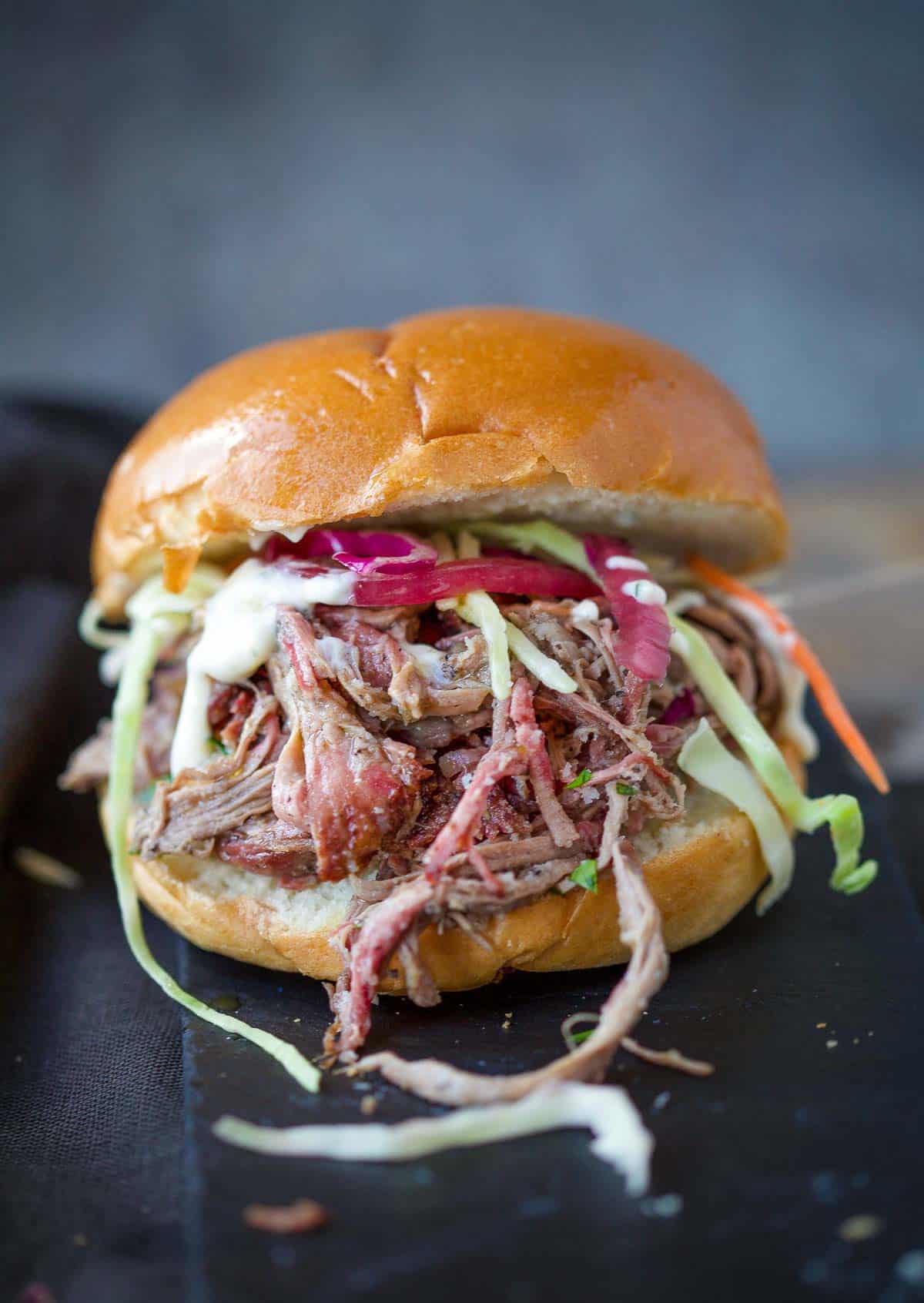 A smoked pulled lamb slider sandwich topped with pickled onions and coleslaw