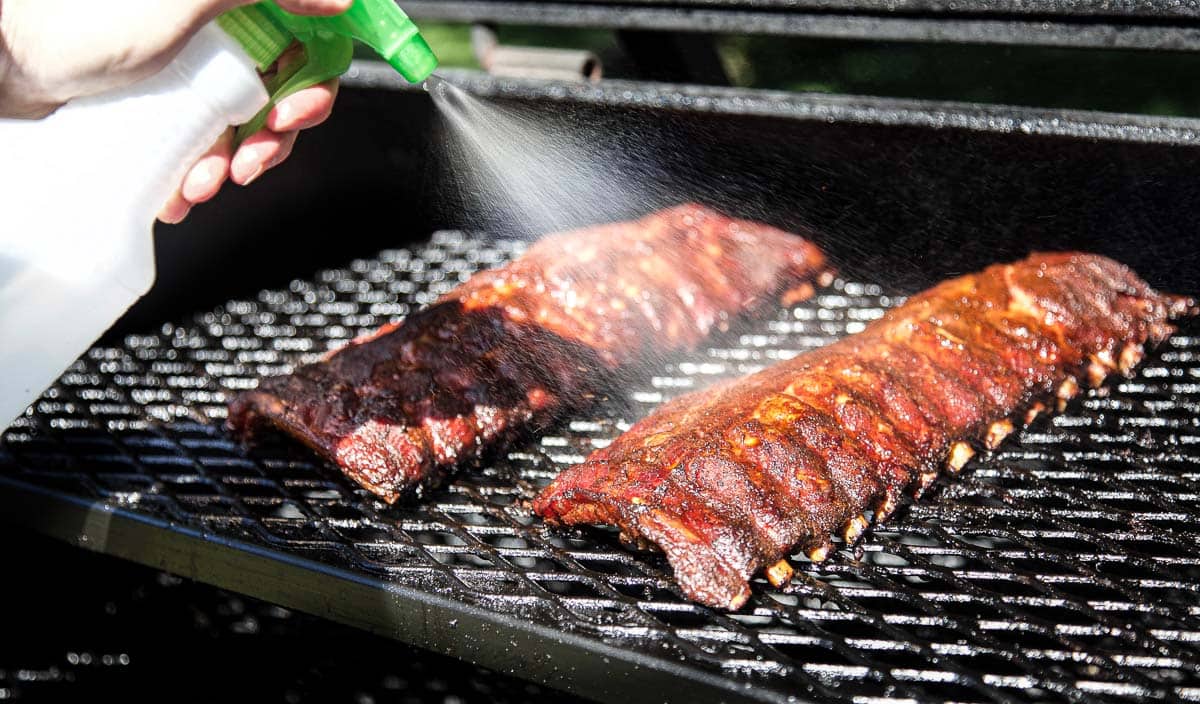 Spritzing pork ribs using a spray bottle on an offset smoker.