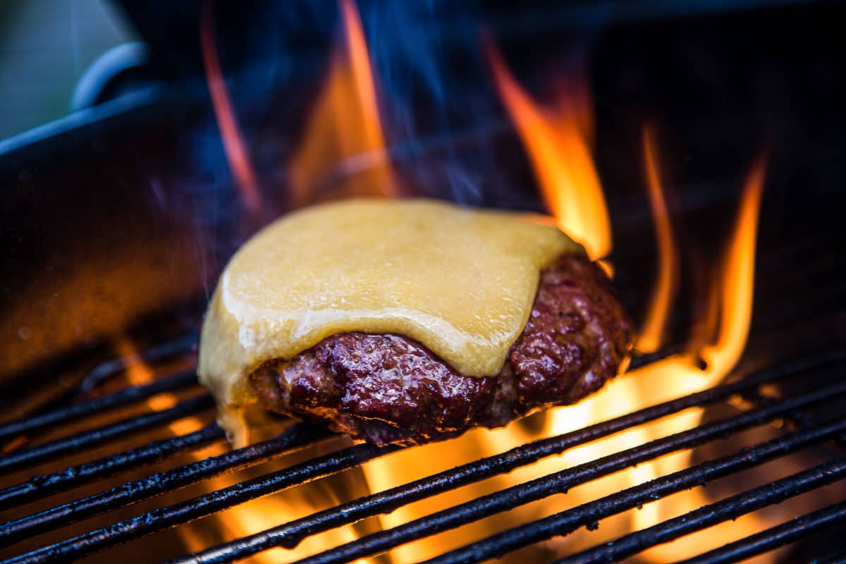 A cheeseburger cooking on the grill over direct flames