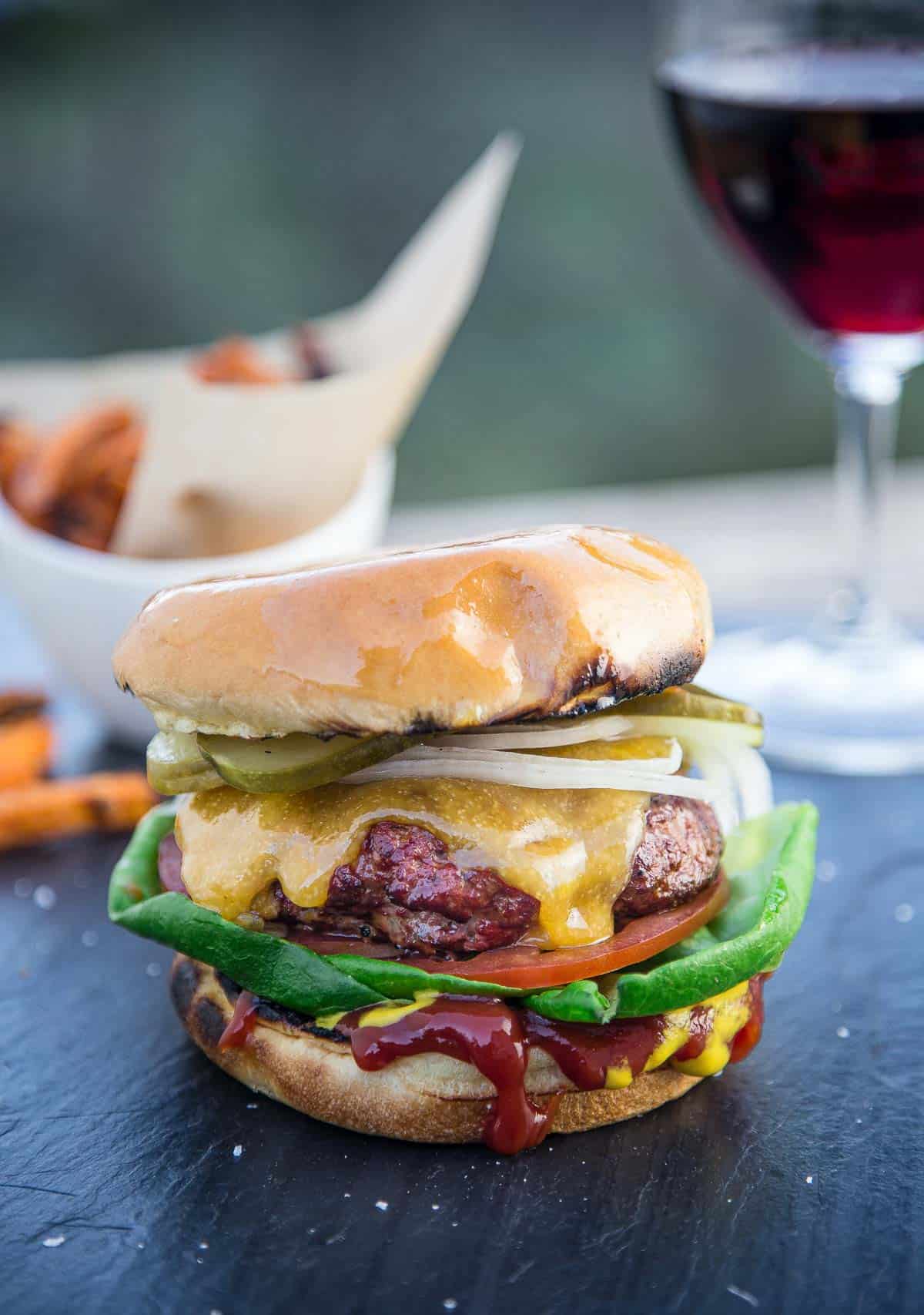 A classic All American Cheeseburger on a serving platter with a glass of wine and fries