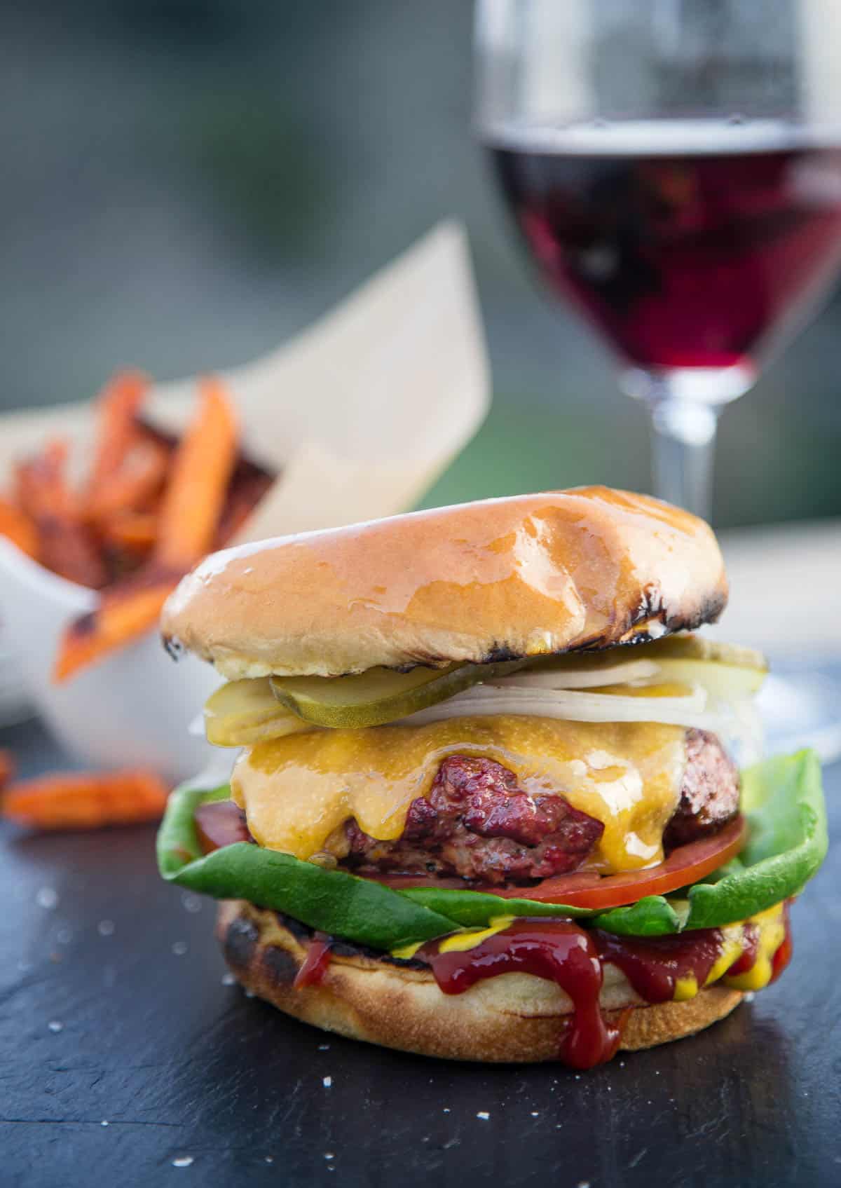 A cheeseburger with a glass of wine in the background