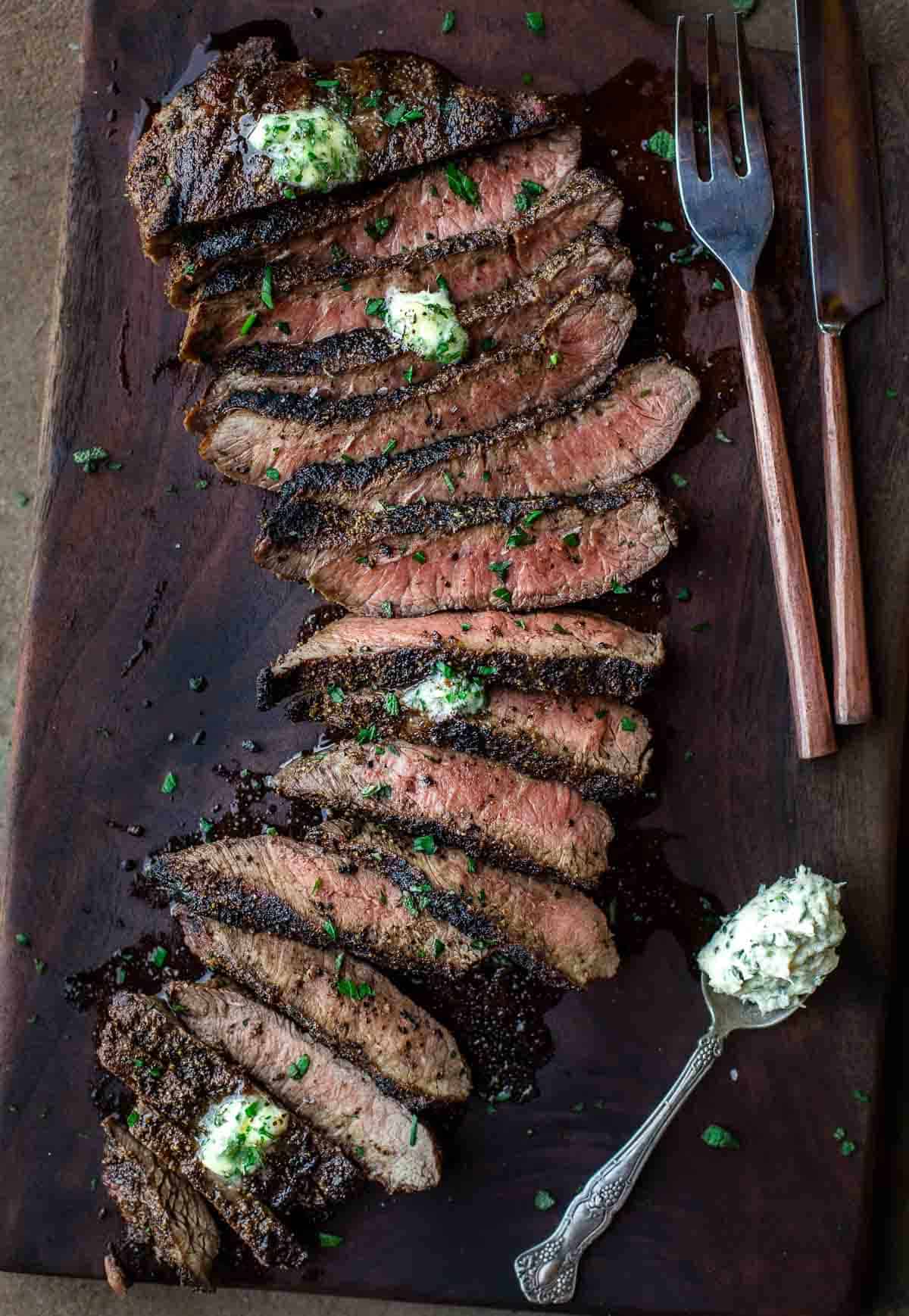 A grilled flat iron steak topped with compound butter on a cutting board