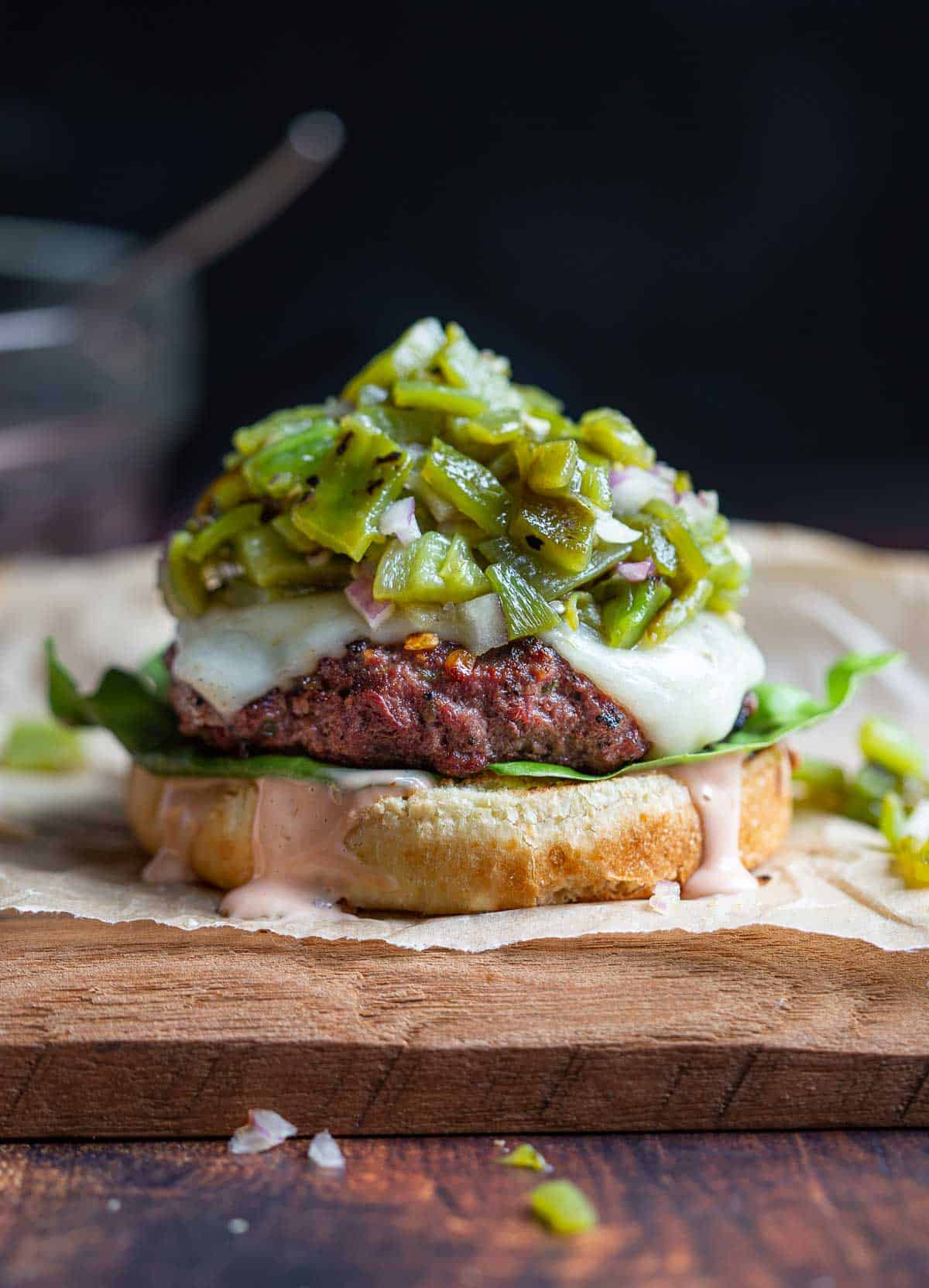 A cheeseburger topped with green chile salsa without a bun top