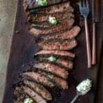 Grilled Flat Iron Steak topped with herb butter on a cutting board