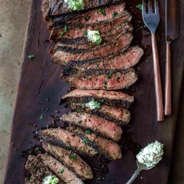 Grilled Flat Iron Steak topped with herb butter on a cutting board