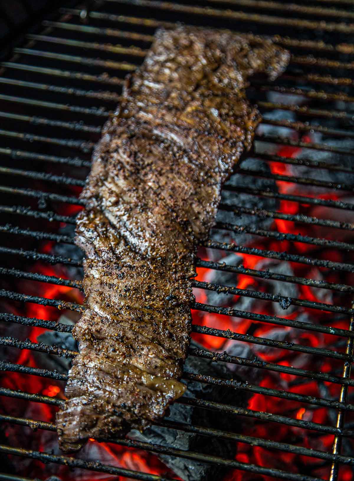 Skirt steak being grilled direct over charcoal.