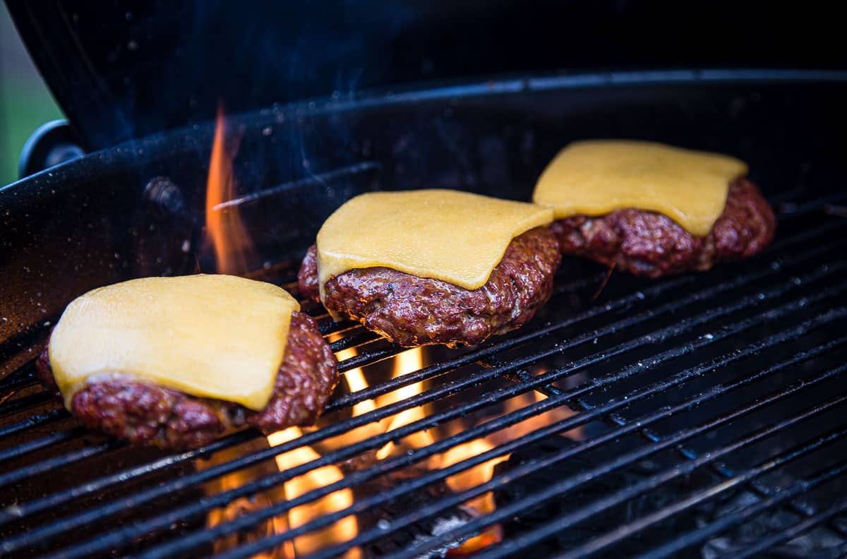 Three cheeseburgers cooking on a grill over fire