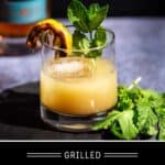 A Grilled Lemon Whiskey Smash in a glass and garnished with a grilled lemon wedge and fresh mint