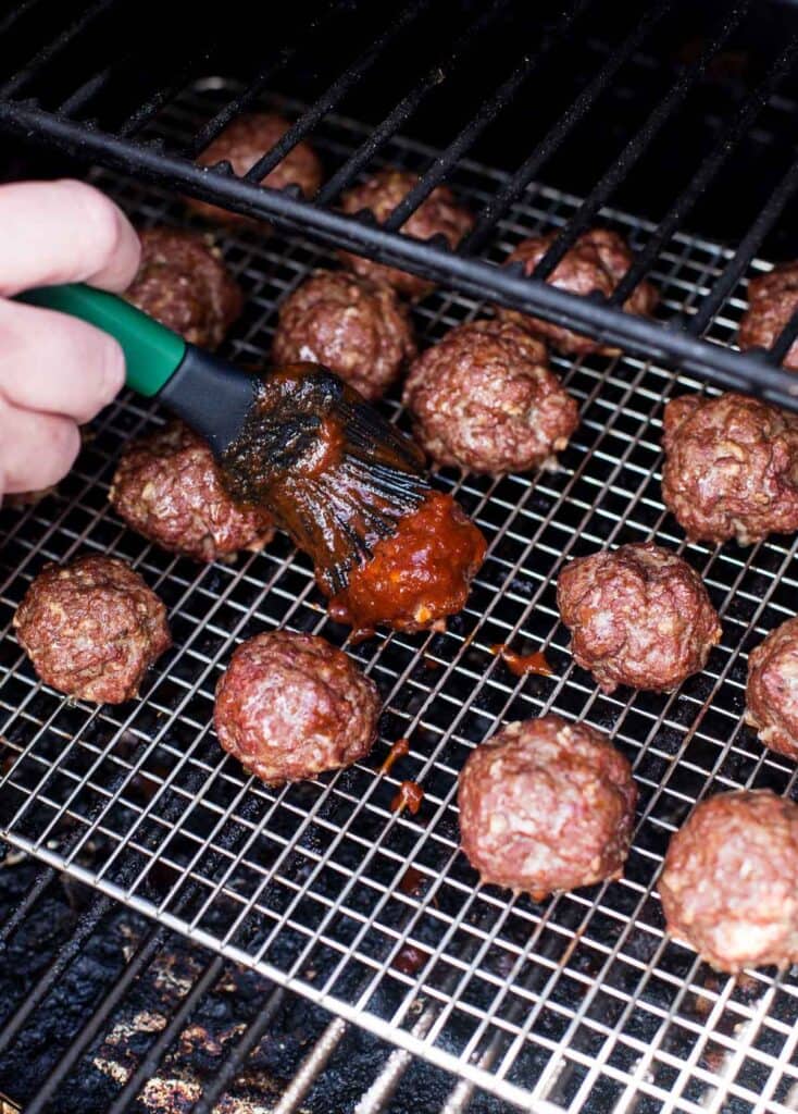 Glazing BBQ meatballs with a silicone brush on a pellet grill.