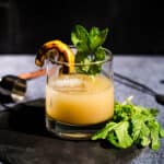 A Grilled Lemon Whiskey Smash in a glass with a lemon garnish and fresh mint