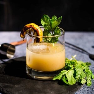 A Grilled Lemon Whiskey Smash in a glass with a lemon garnish and fresh mint