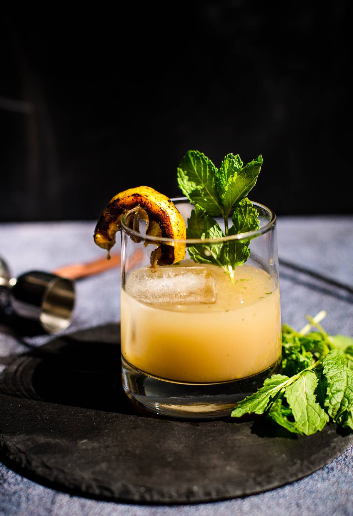 A Grilled Lemon Whiskey Smash in a glass with a lemon and mint garnish 