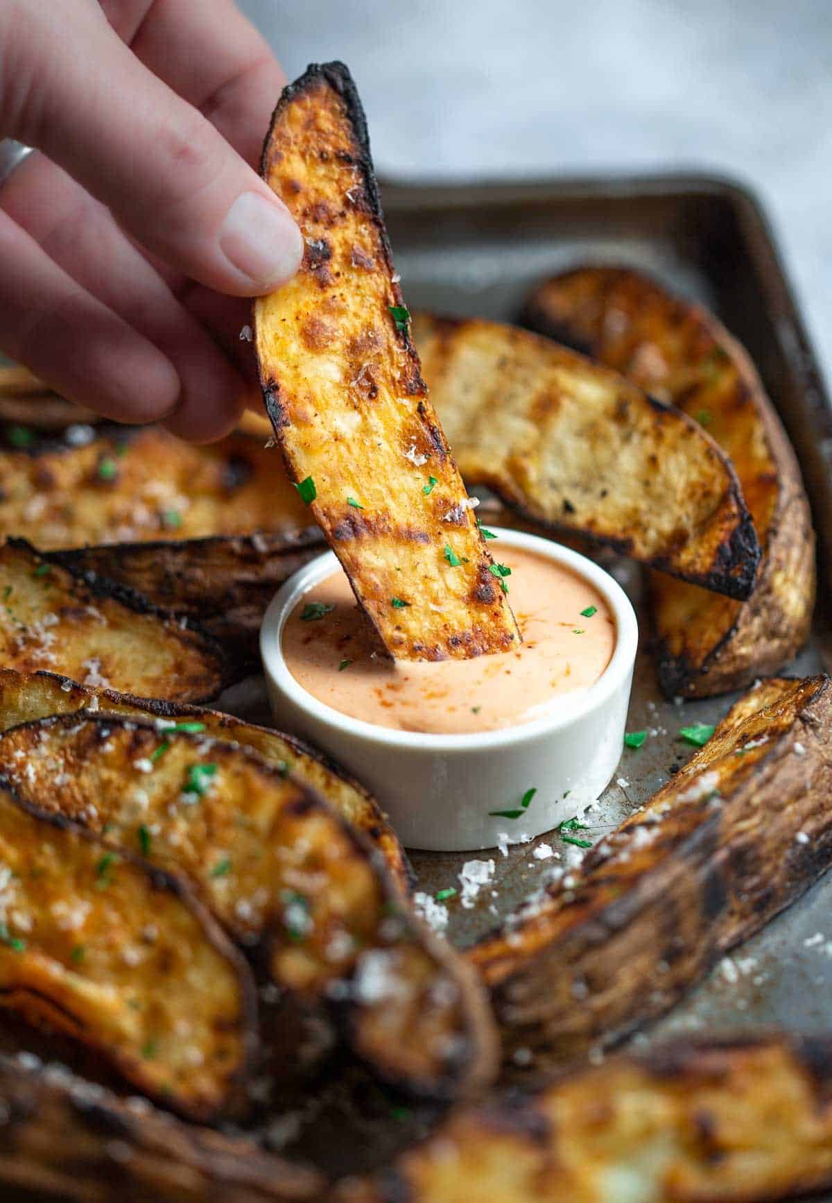 Potato wedges being dipped in a classic fry sauce on a platter.