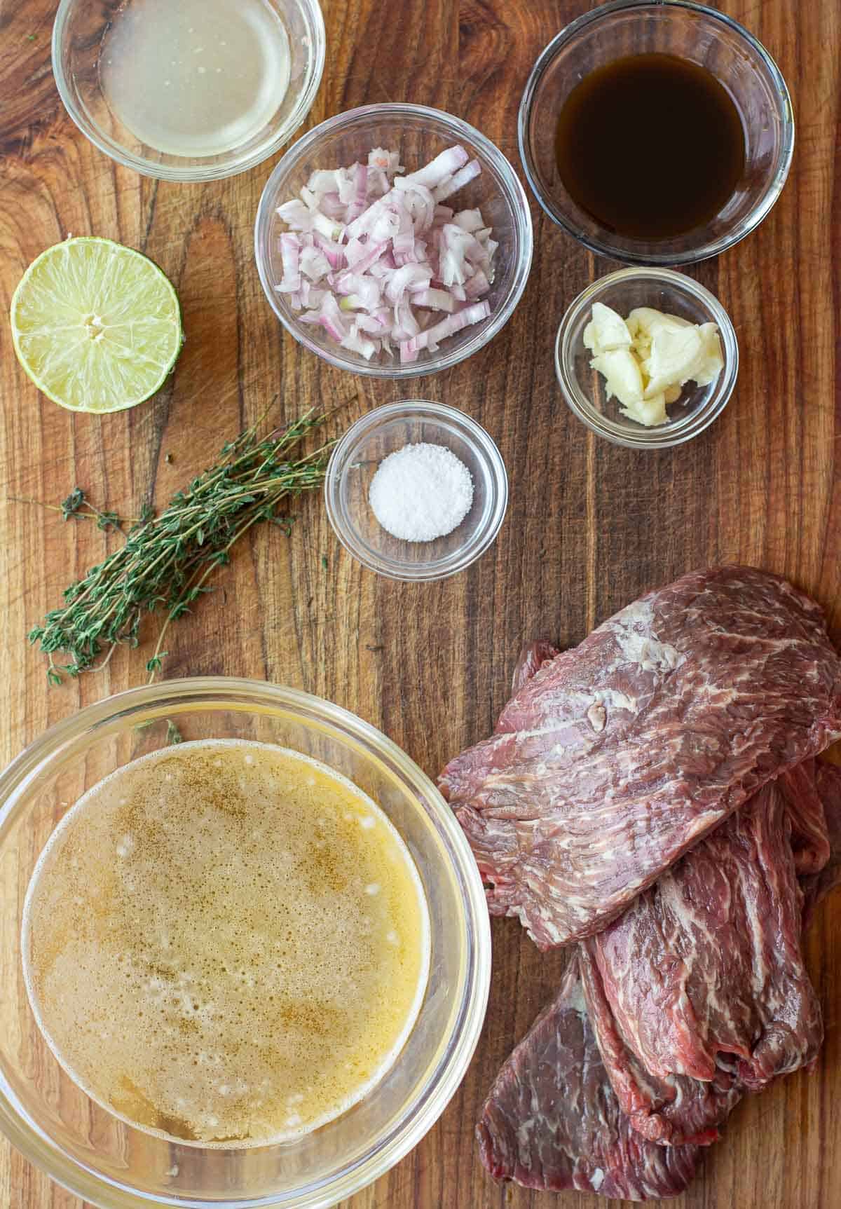 Beer Beef Marinade ingredients on a cutting board including beer, lime juice, Worcestershire, garlic, shallots, and bavette steak.