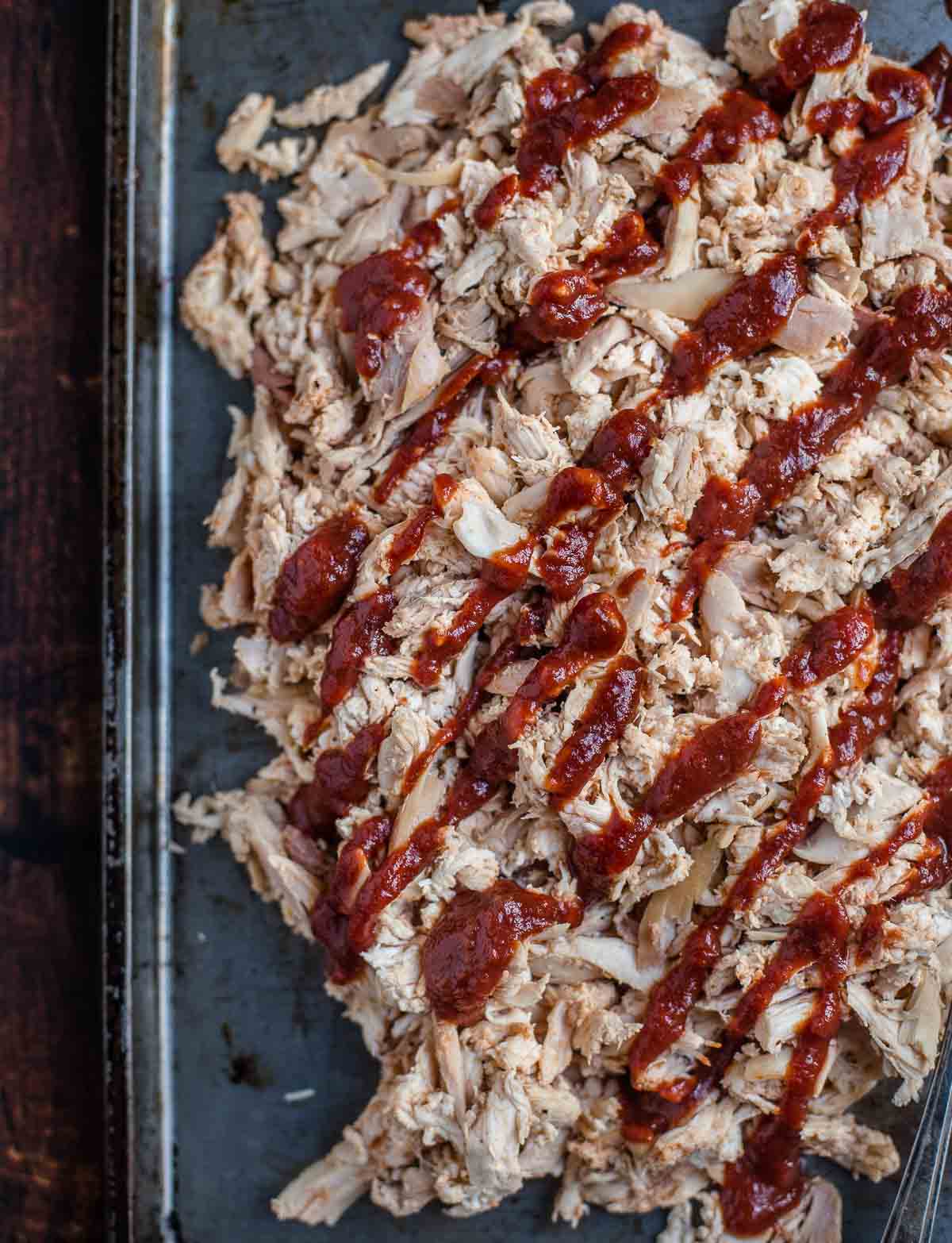 Pulled shredded smoked chicken on a serving platter topped with red wine BBQ sauce