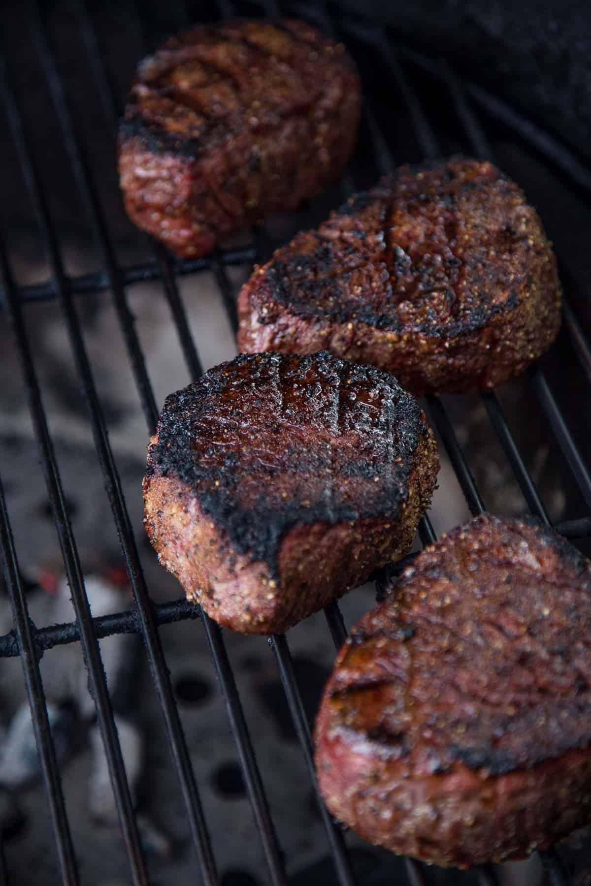 Four filet mignon steaks cooking on the grill.