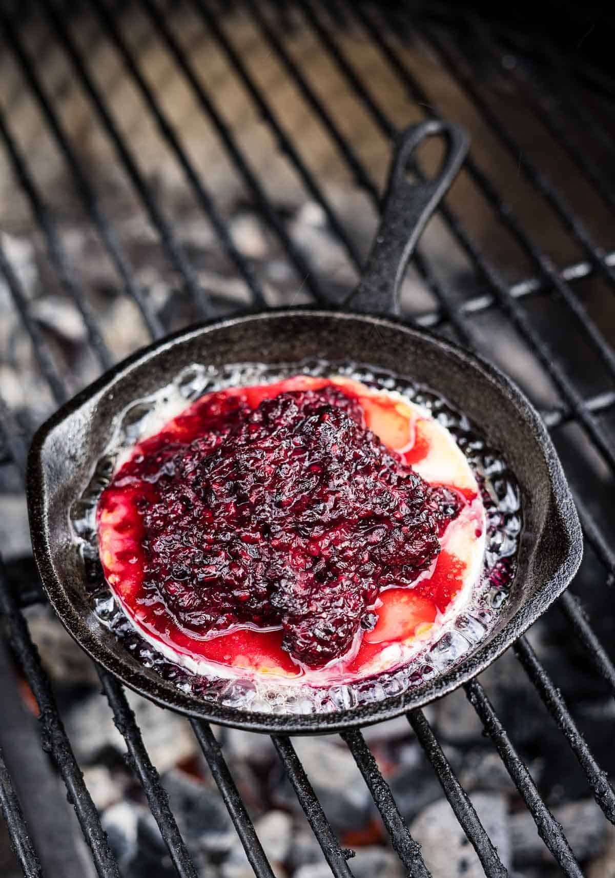 baked brie with blackberry jam in a cast iron pan on the grill