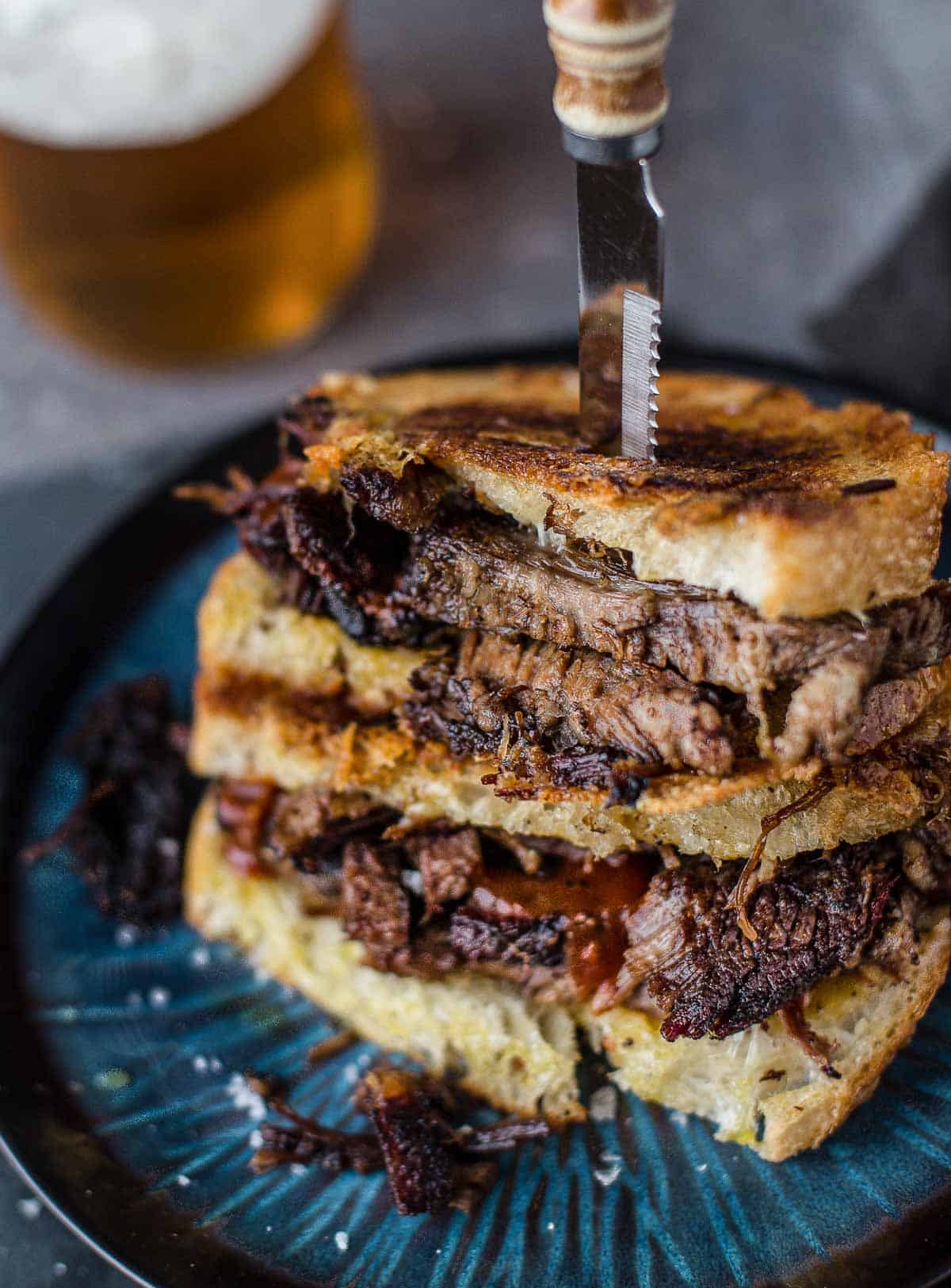 A brisket grilled cheese sandwich with a glass of beer 