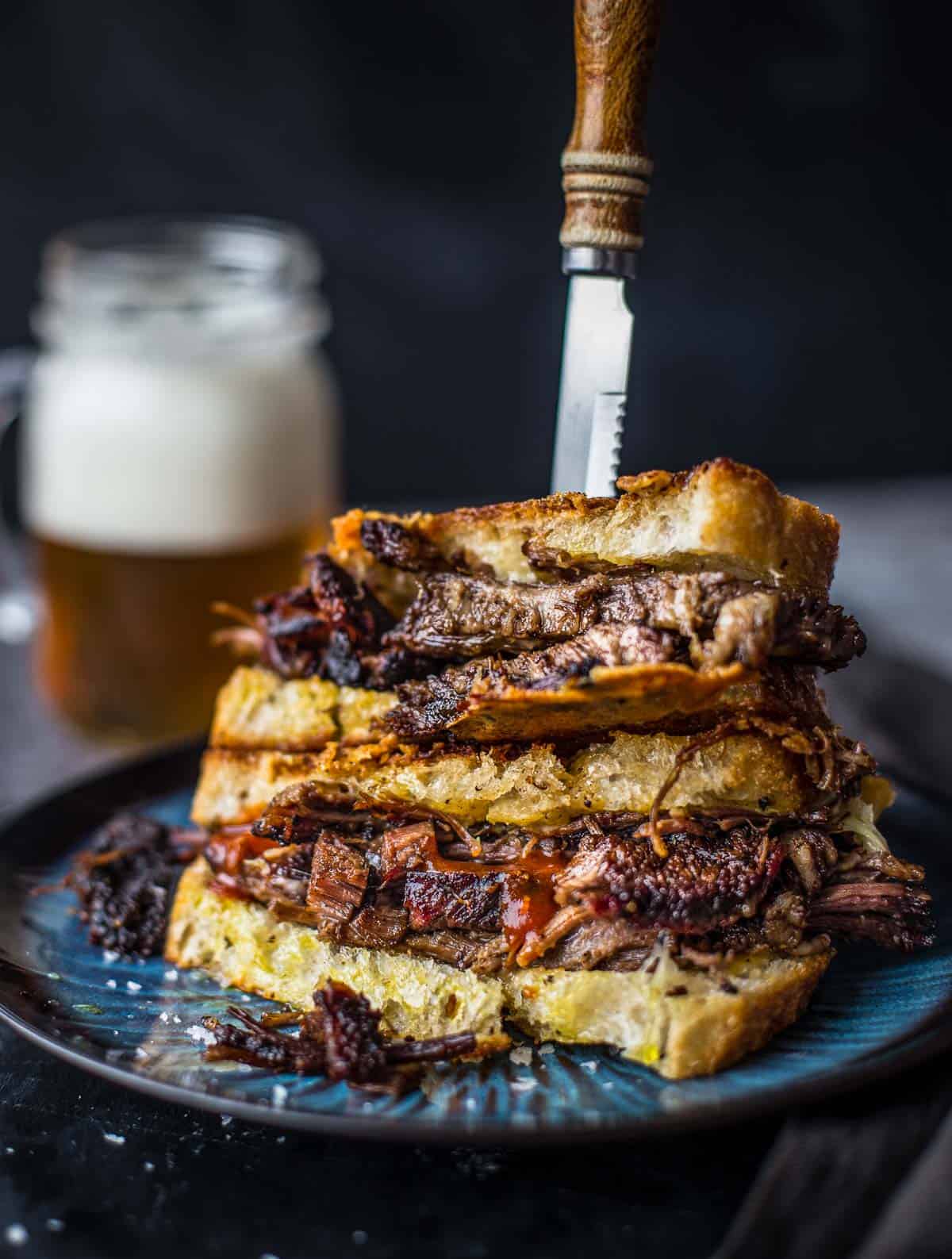 Two Brisket Grilled Cheese Sandwich halves on top of each other with a glass of beer in the background