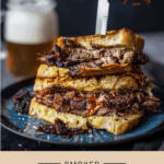 Two Brisket Grilled Cheese Sandwich halves on top of each other with a glass of beer in the background