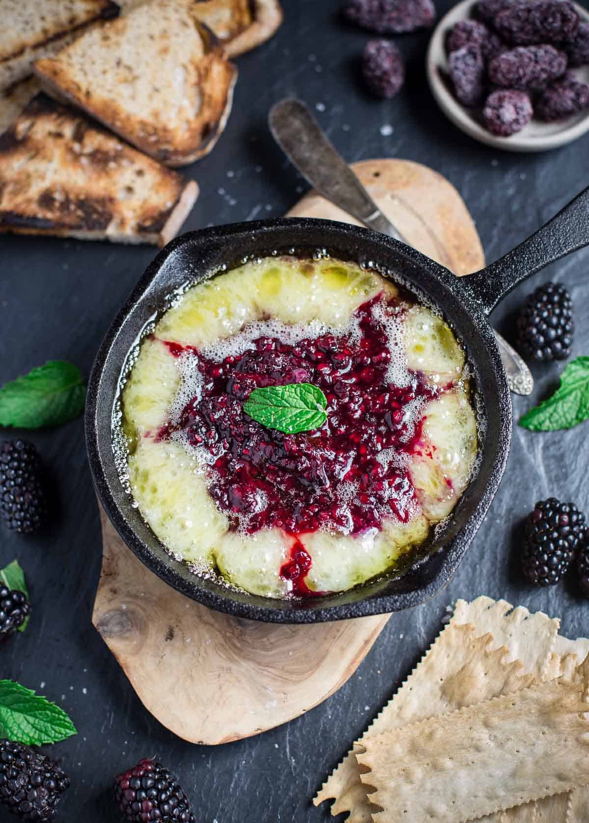 Grilled Brie with Blackberry Jam in a serving dish with crackers and grilled bread