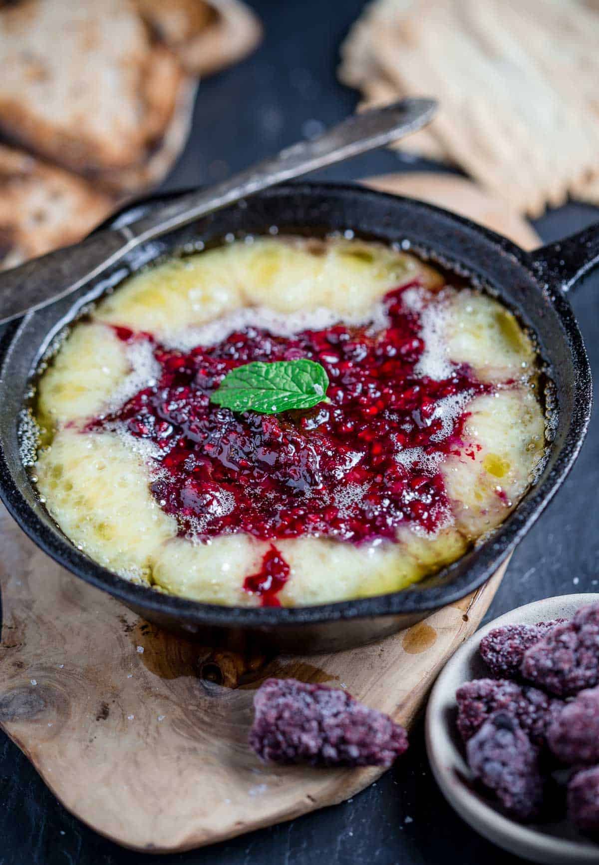 Grilled Baked Brie with Blackberry Jam on a serving dish with crackers and bread.