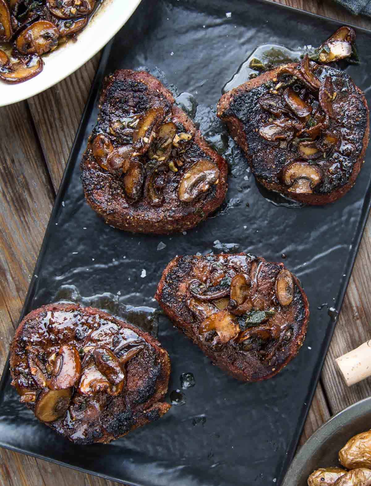 grilled filet mignon steaks topped with mushroom brown butter pan sauce on a serving platter