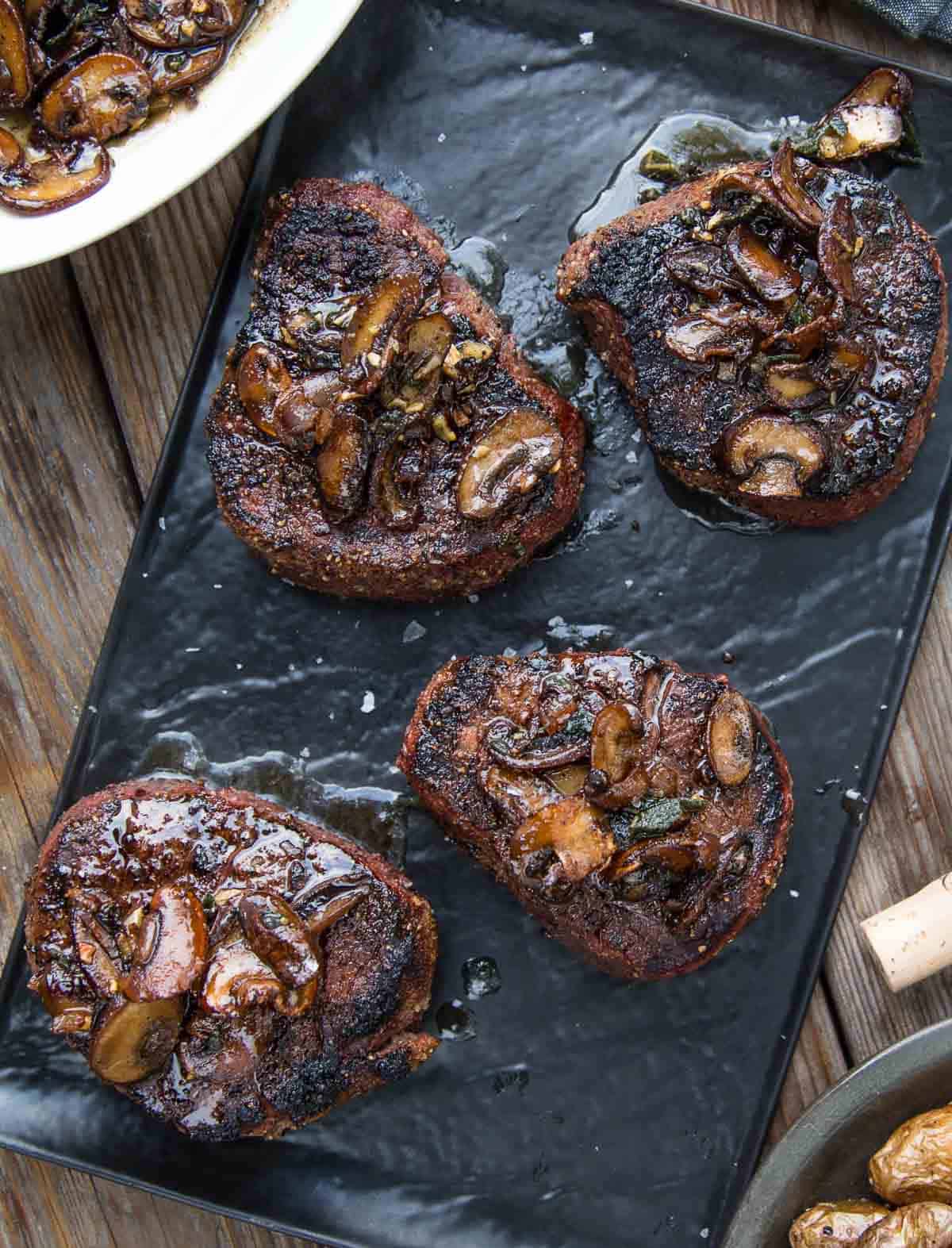 Grilled filet mignon steaks topped with mushroom brown butter pan sauce on a serving platter.