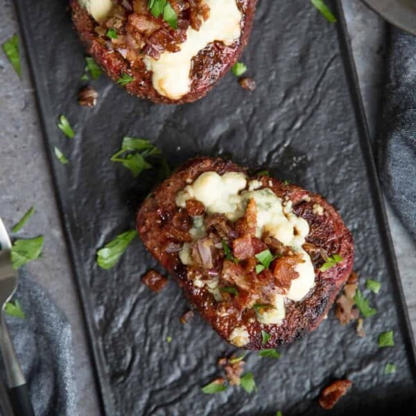 Perfectly cooked filet mignon topped with blue cheese, bacon, and caramelized onions on a serving platter.