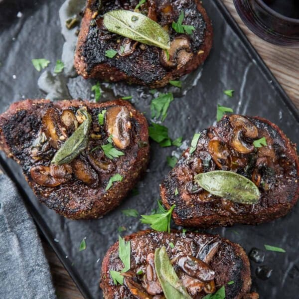 Four grilled filet mignon steaks topped with a mushroom brown butter sauce on a platter with wine pairing