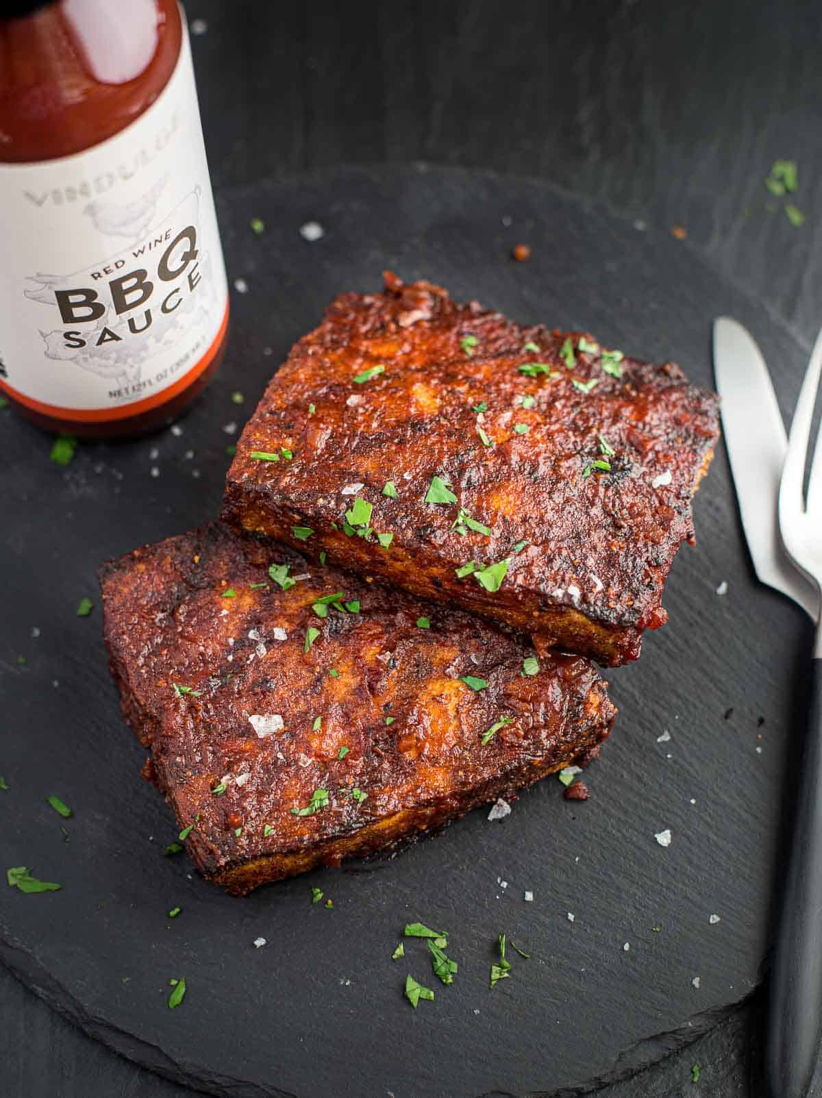 Two Grilled Tofu steaks topped with a red wine BBQ Sauce with a jar of Vindulge Red Wine BBQ Sauce on a platter