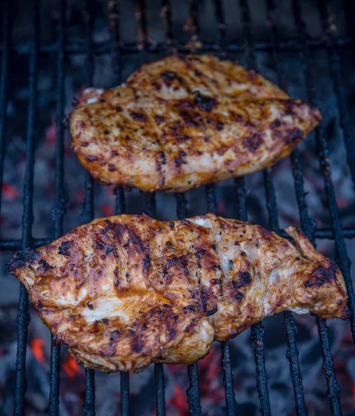 Two marinated chicken breasts cooking on a hot grill