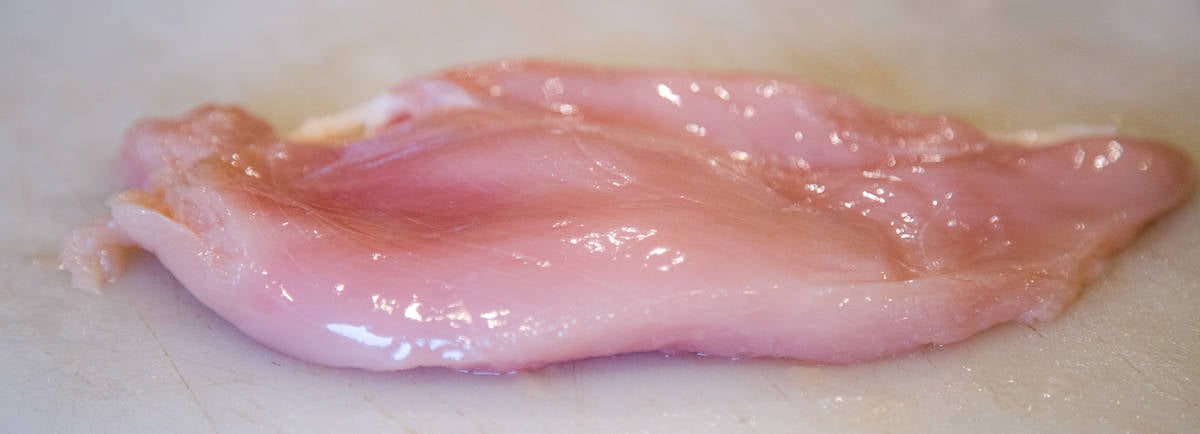 a raw chicken breast on a cutting board after being pounded for consistency