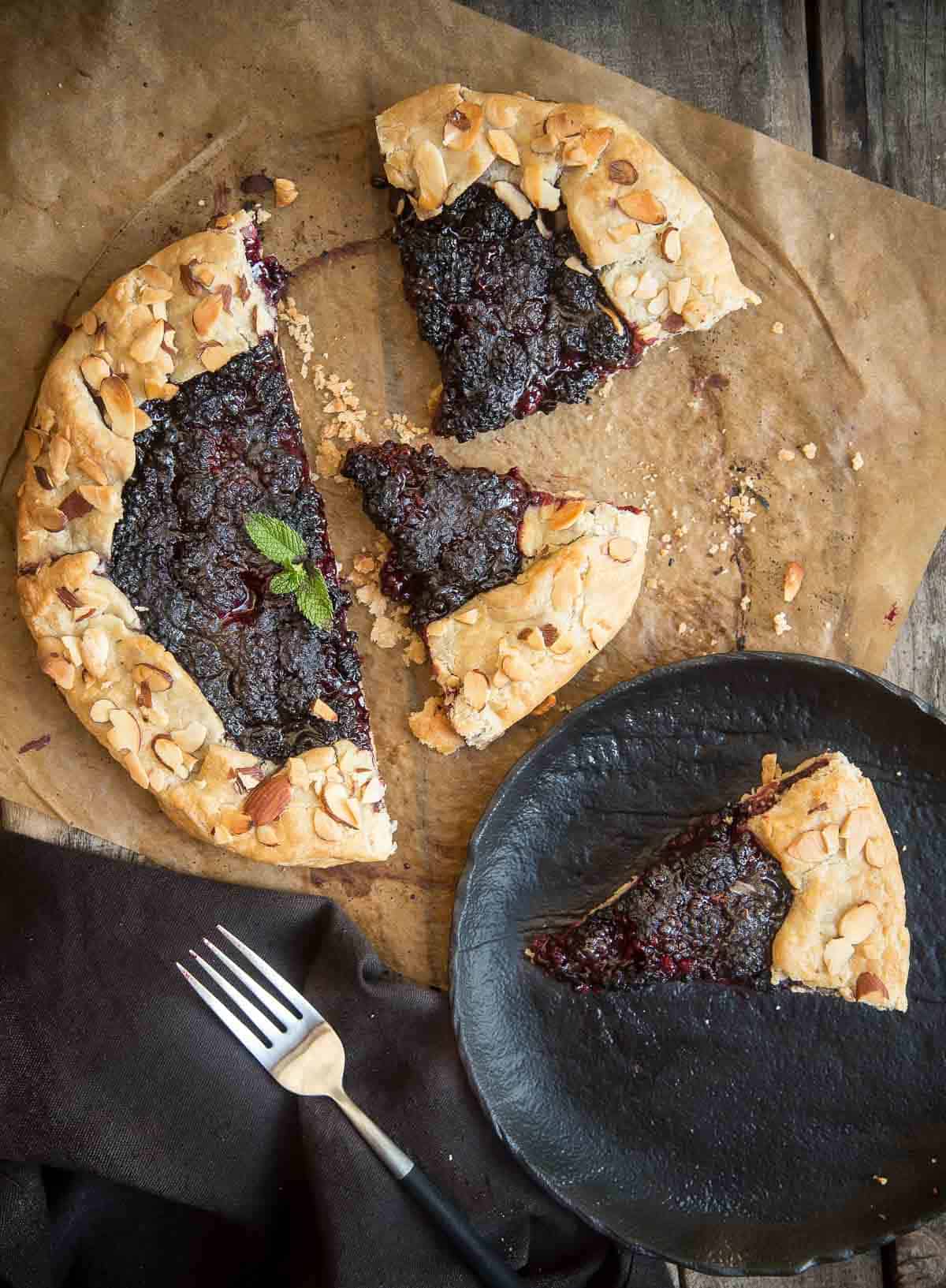A grilled blackberry crostata on a serving platter with a slice of blackberry crostata on a plate