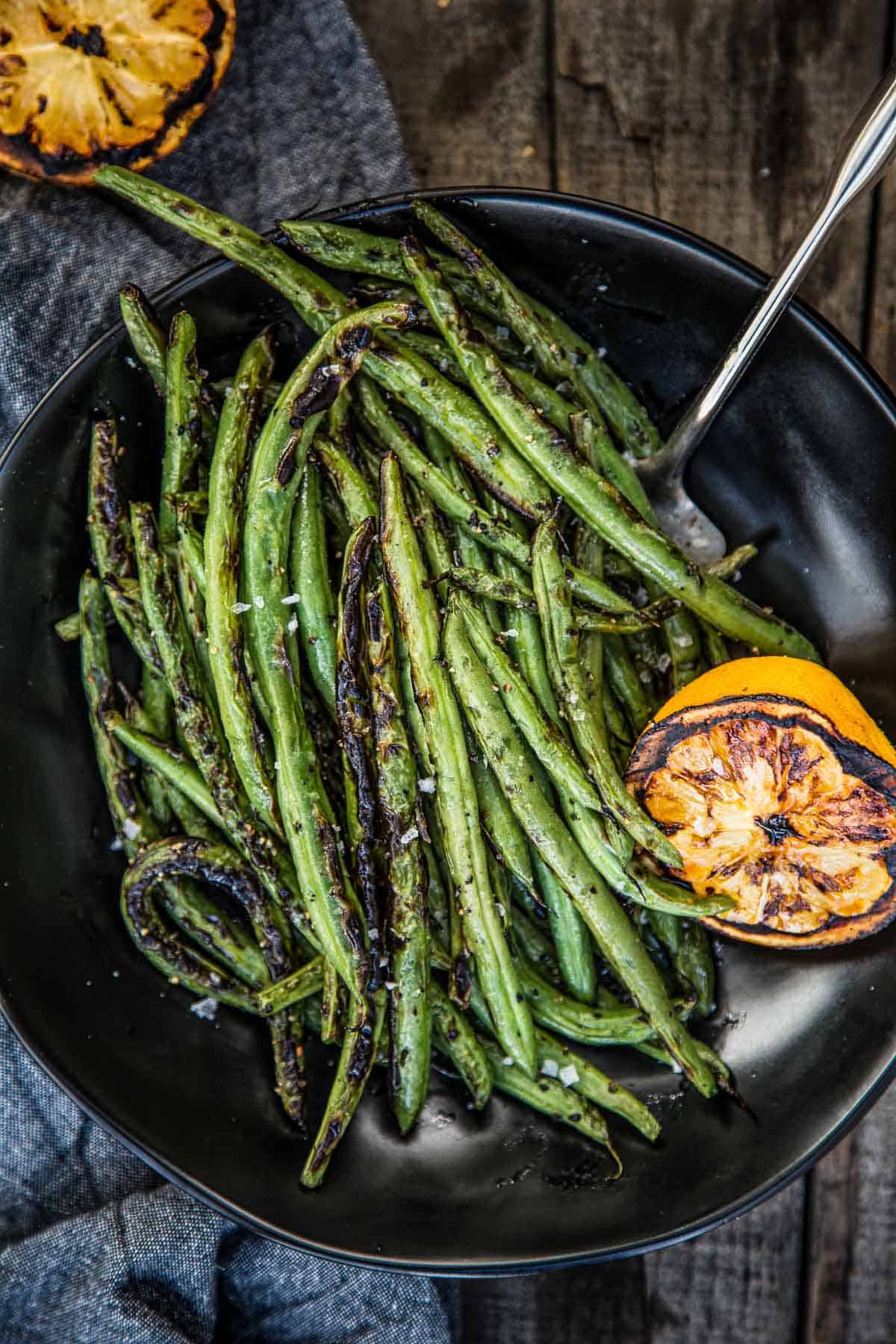 Grilled Green Beans on a platter with slices of grilled lemon