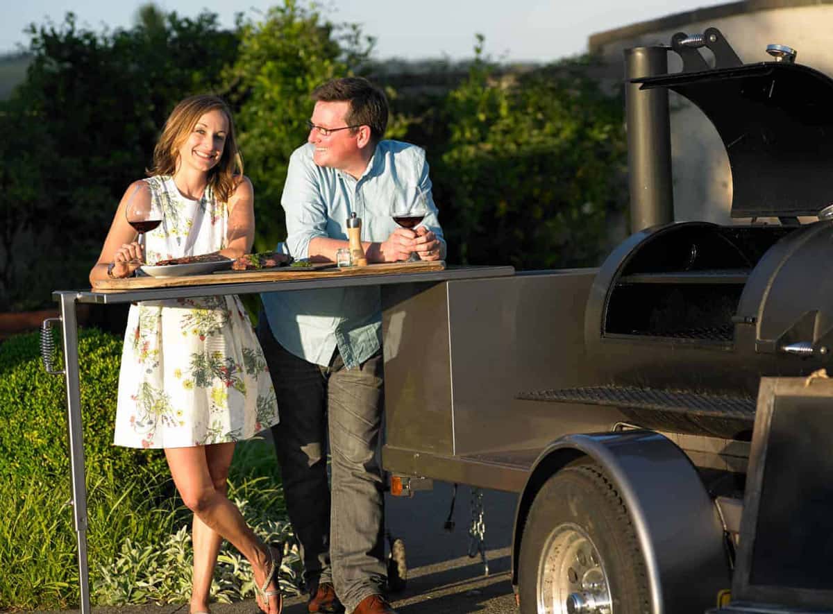 Mary Cressler and Sean Martin of Vindulge in front of a large offset smoker