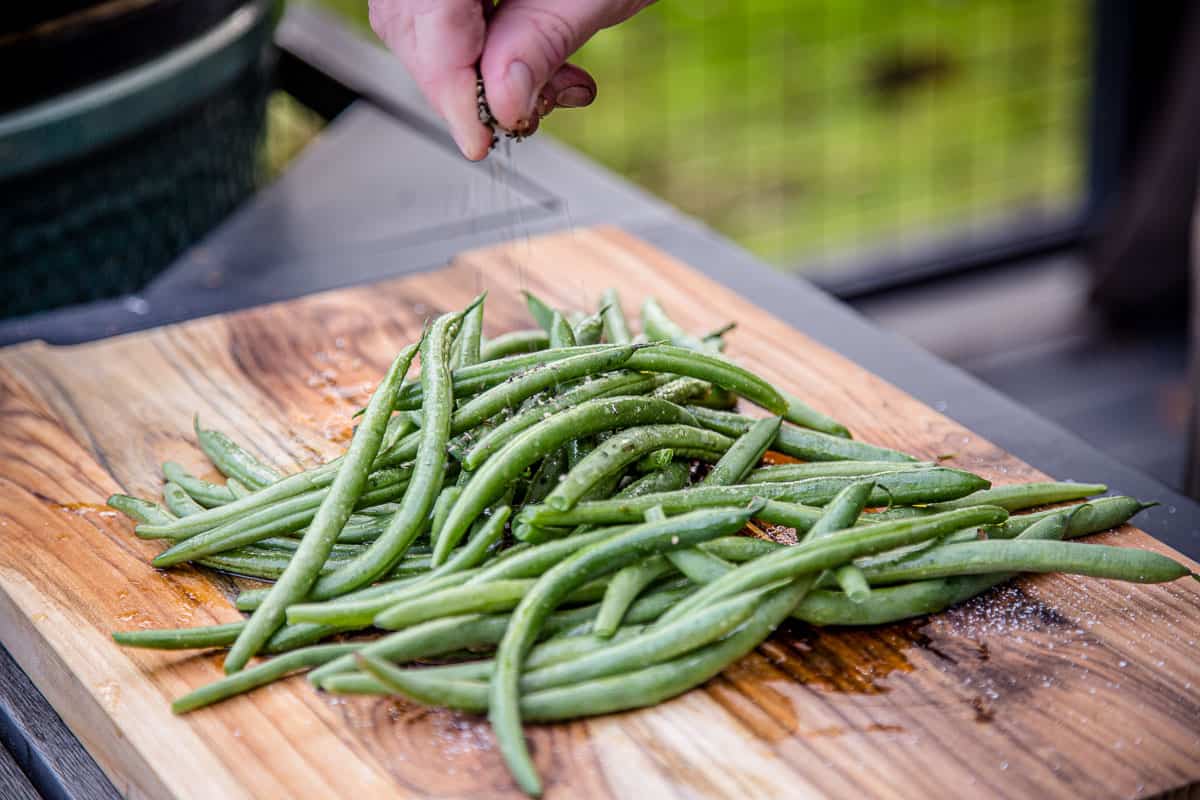 green beans on a cutting board being seasoned with salt and pepper