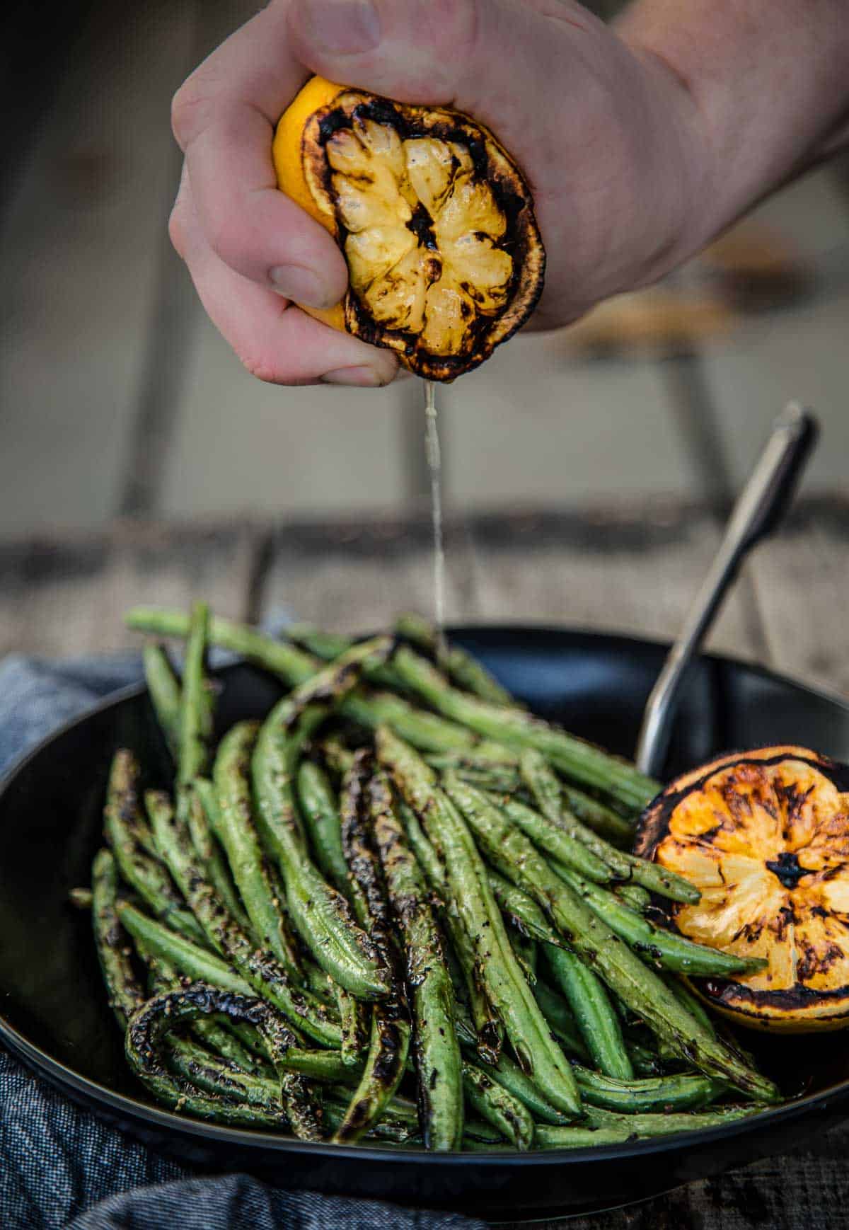Grilled Green Beans on a platter being topped with grilled lemon juice