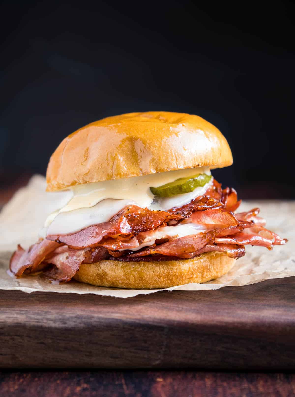 A fried mortadella sandwich layered with smoked mortadella slices, provolone cheese, and a lemon aioli on a brioche bun on a cutting board.