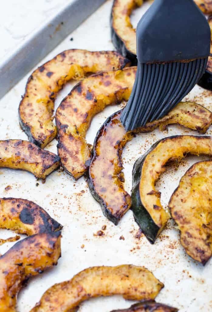 grilled acorn squash slices being glazed with maple syurup