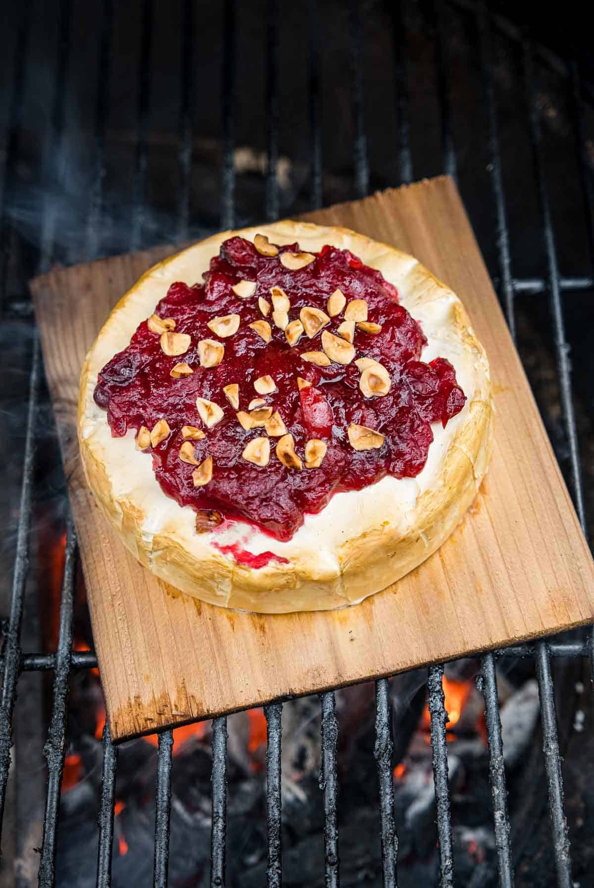 Cedar plank brie with Cranberry Sauce grilling over direct heat on a big green egg grill.