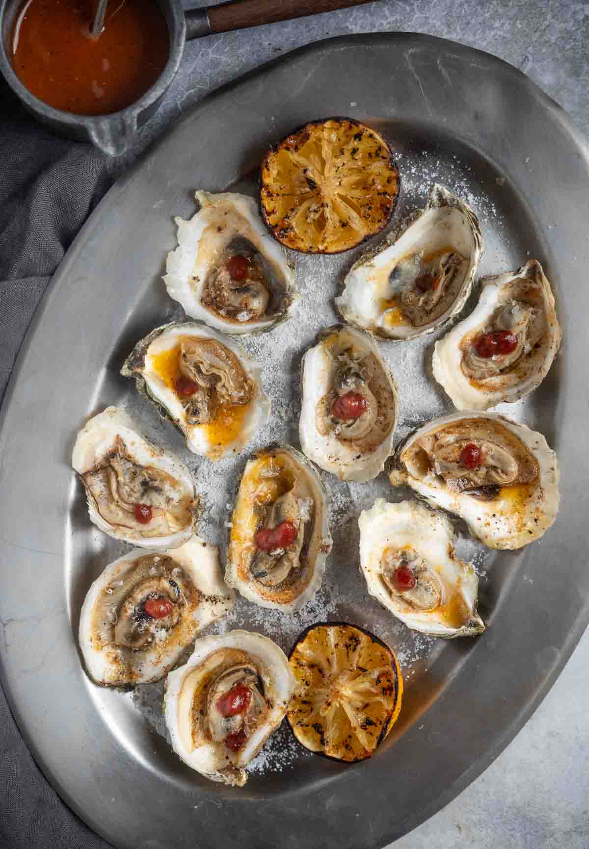 BBQ Oysters in the half shell on a serving platter. The kosher salt is laid out to hold the oysters in place.
