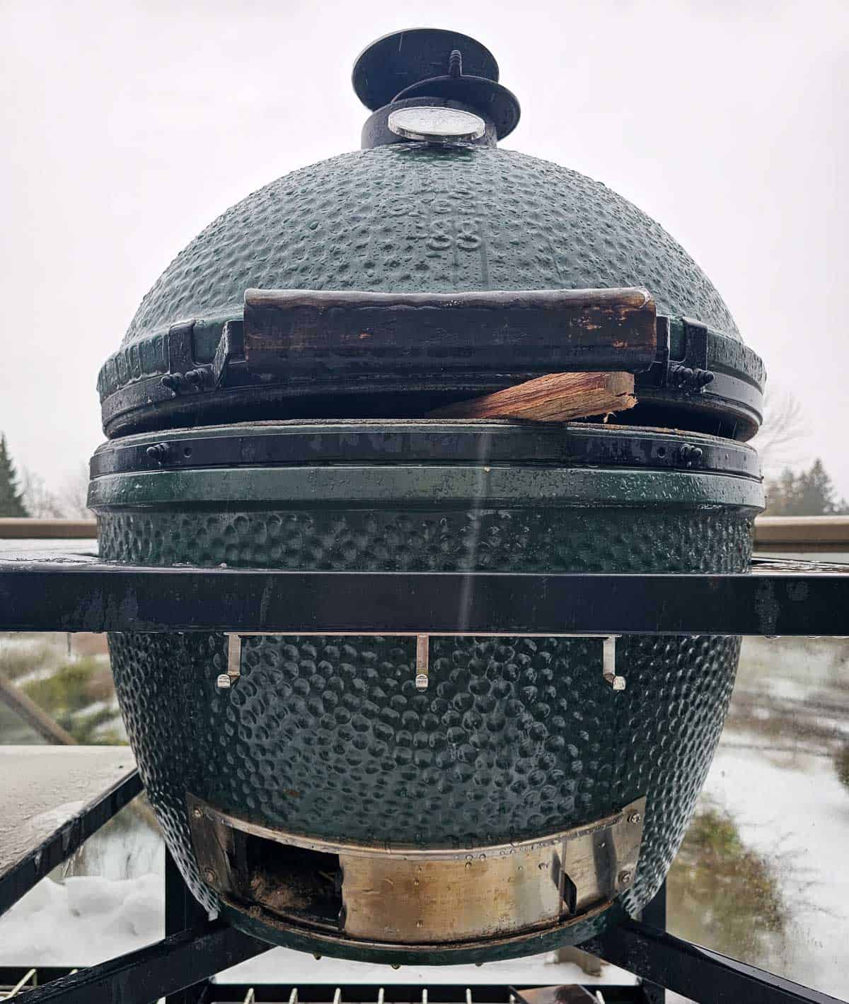 A Big Green Egg with the lid slightly open with wood