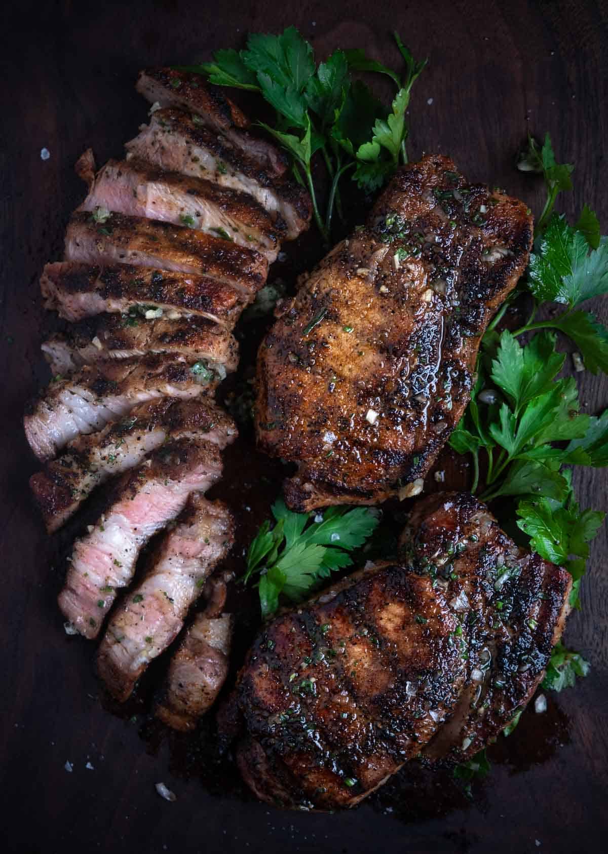 a grilled pork chop sliced into slices, alongside of two grilled whole pork chops on a platter