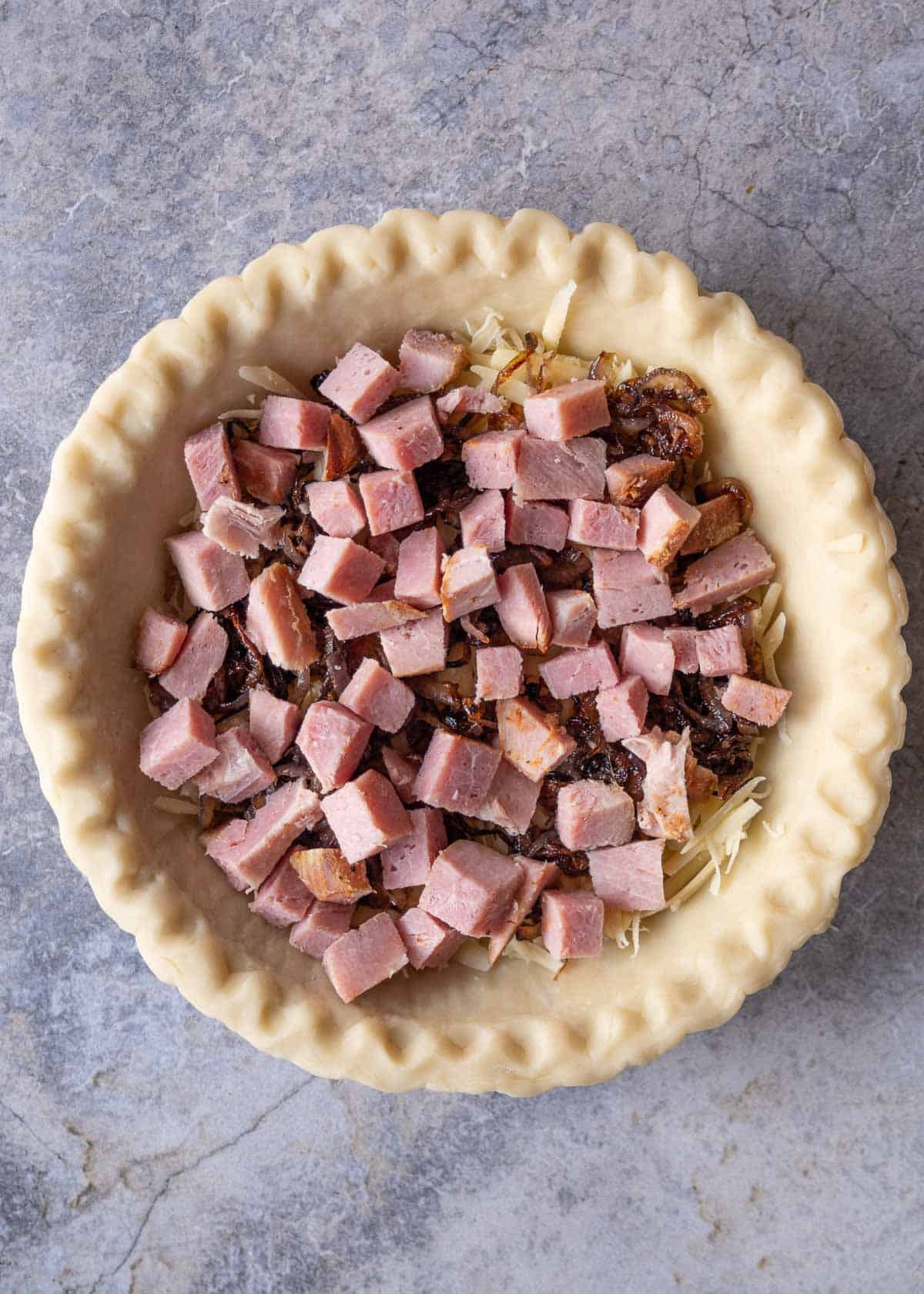 layering ingredients into a pie crust to make a ham quiche